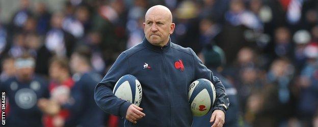Shaun Edwards frowns holding two rugby balls