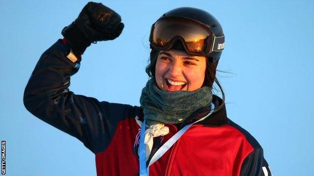 Huckaby punching the air, wearing a snowboarding helmet and goggles with a gold medal around her neck