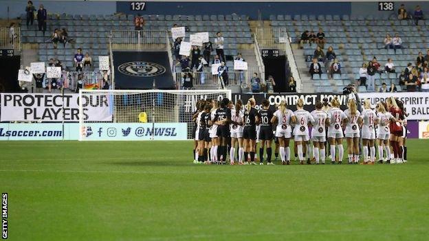 NJ/NY Gotham and Washington Spirit players arm-in-arm in a circle in a gesture of solidarity