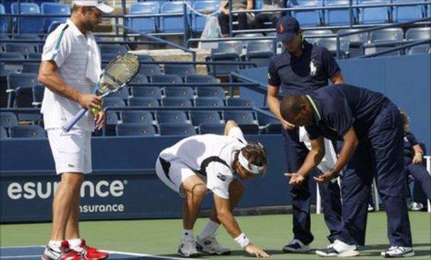 David Ferrer examines the spot where water is seeping on to the court