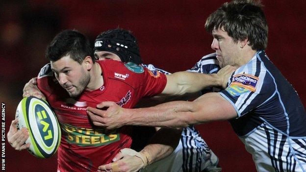 Scarlets' Dan Newton tries to break the tackle of Blues Michael Paterson and James Down