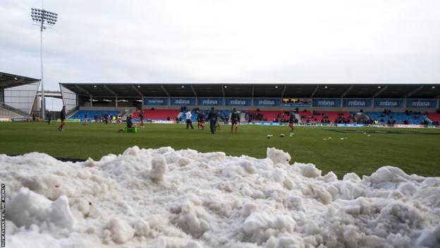 Scarlets players warm up for their LV= Cup match against Sale Sharks with snow piled around the Salford City Stadium pitch.
