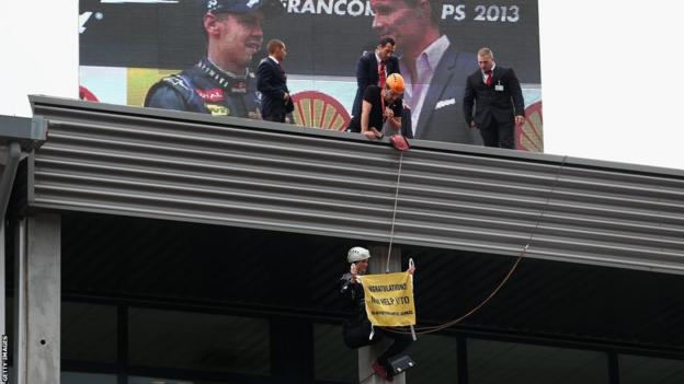 A protestor abseils from the roof to unveil a flag above the podium