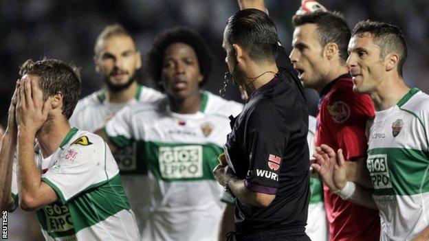 Elche's players protest as referee Cesar Muniz shows a yellow card to Ruben Perez