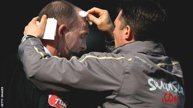 Referee Mike Dean receiving treatment from a member of Swansea City's medical staff after being struck by a coin at Ninian Park in 2009