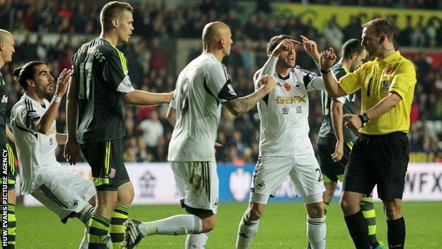 Swansea players show their disbelief after referee Robert Madley awards a late penalty to Stoke