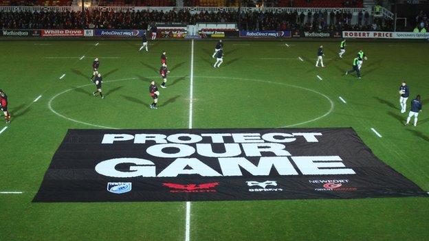 Dragons and Blues players warm up before their match after a protest banner is placed on the pitch