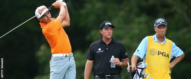 Rickie Fowler swings as Phil Mickelson watches on