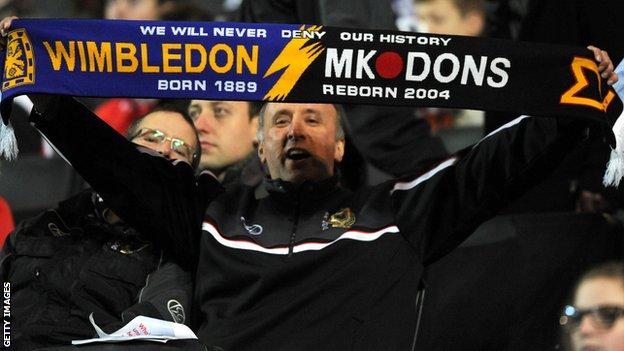 A fan holds an AFC Wimbledon and MK Dons scarf