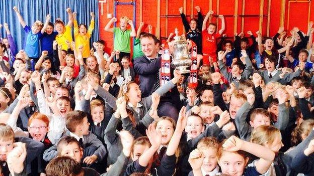The FA Cup being help up and surrounded by happy children