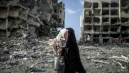 Mujer palestina carga a menor frente a escombros