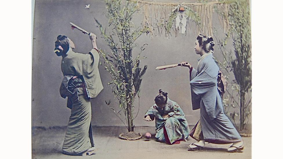 An old photograph of three girls in traditional kimonos playing in a courtyard An old photograph of three girls in traditional kimonos playing in a courtyard