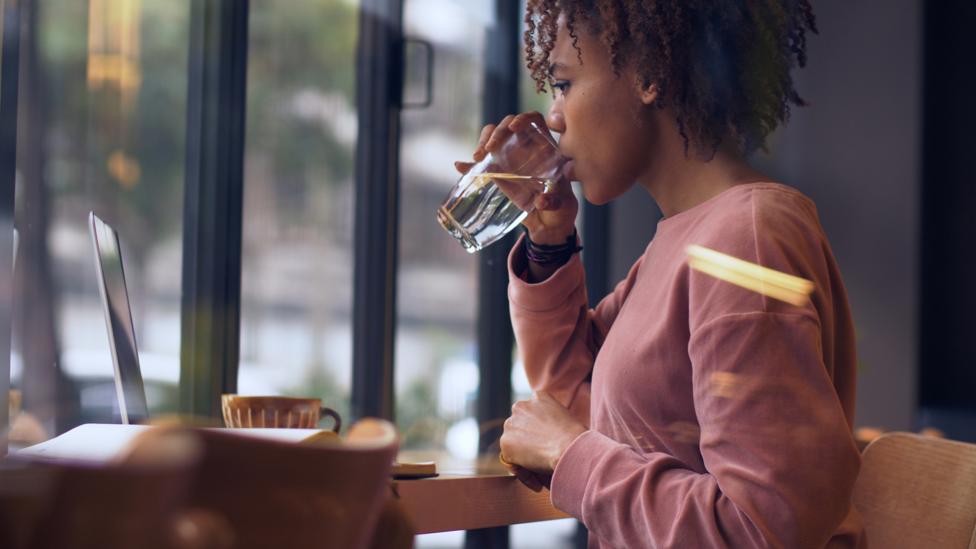 Woman drinking water while working (Credit: Getty Images)