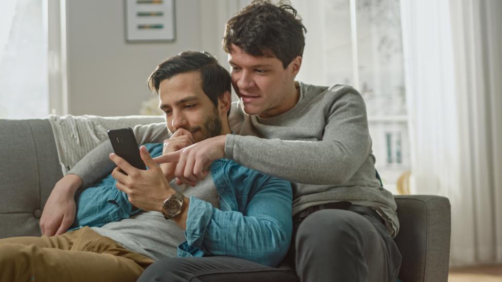 A couple cuddling and looking at a phone screen together (Credit: Getty Images)